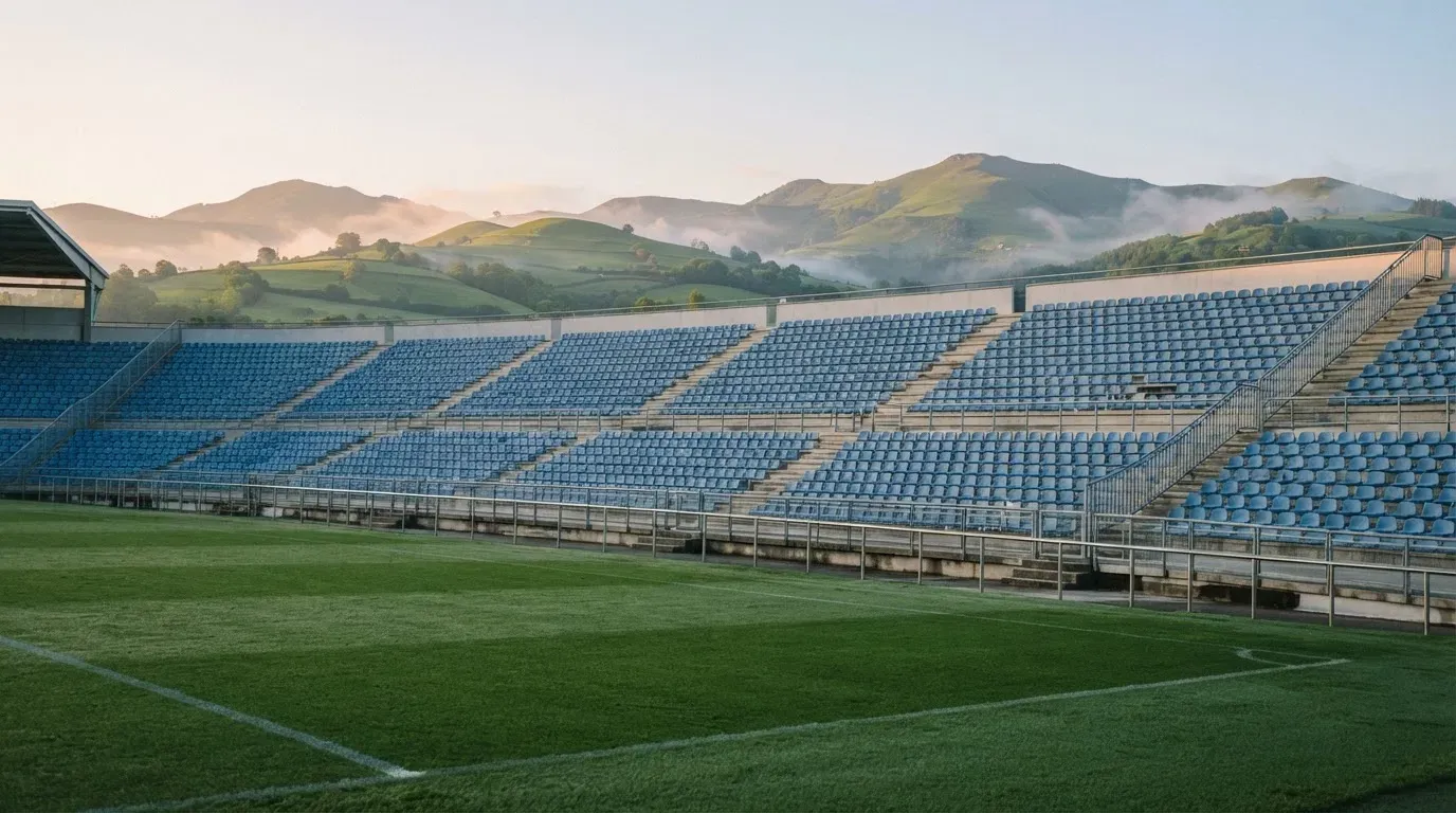 Ein leeres Stadion im Morgenlicht mit Blick auf die Sitzreihen, im Hintergrund Hügel und aufsteigender Nebel.