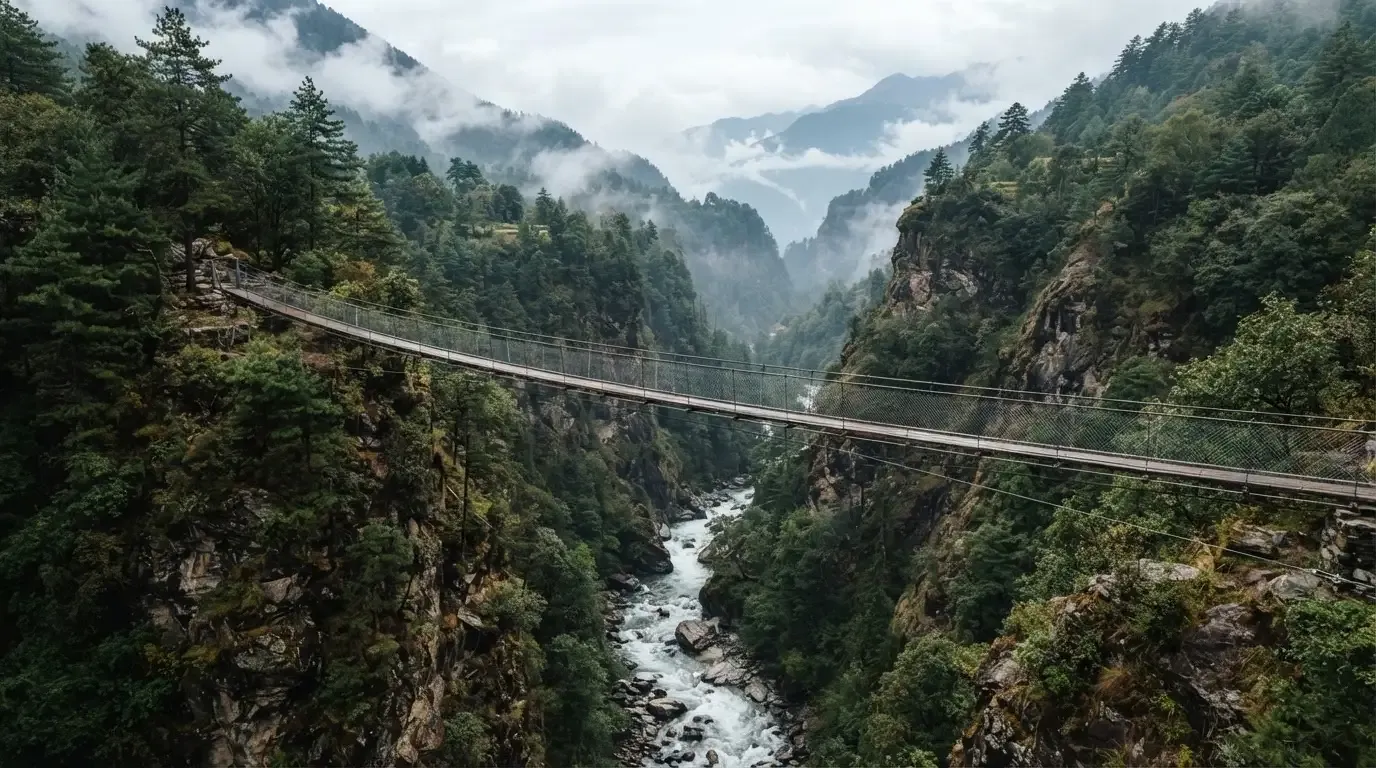 Eine Hängebrücke spannt sich über eine tiefe Schlucht, unten rauscht ein Fluss zwischen bewaldeten Felswänden.
