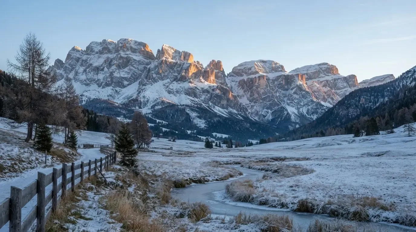Eine verschneite Bergkette erhebt sich über einem stillen Tal, der Himmel darüber ist klar und von blassem Blau.