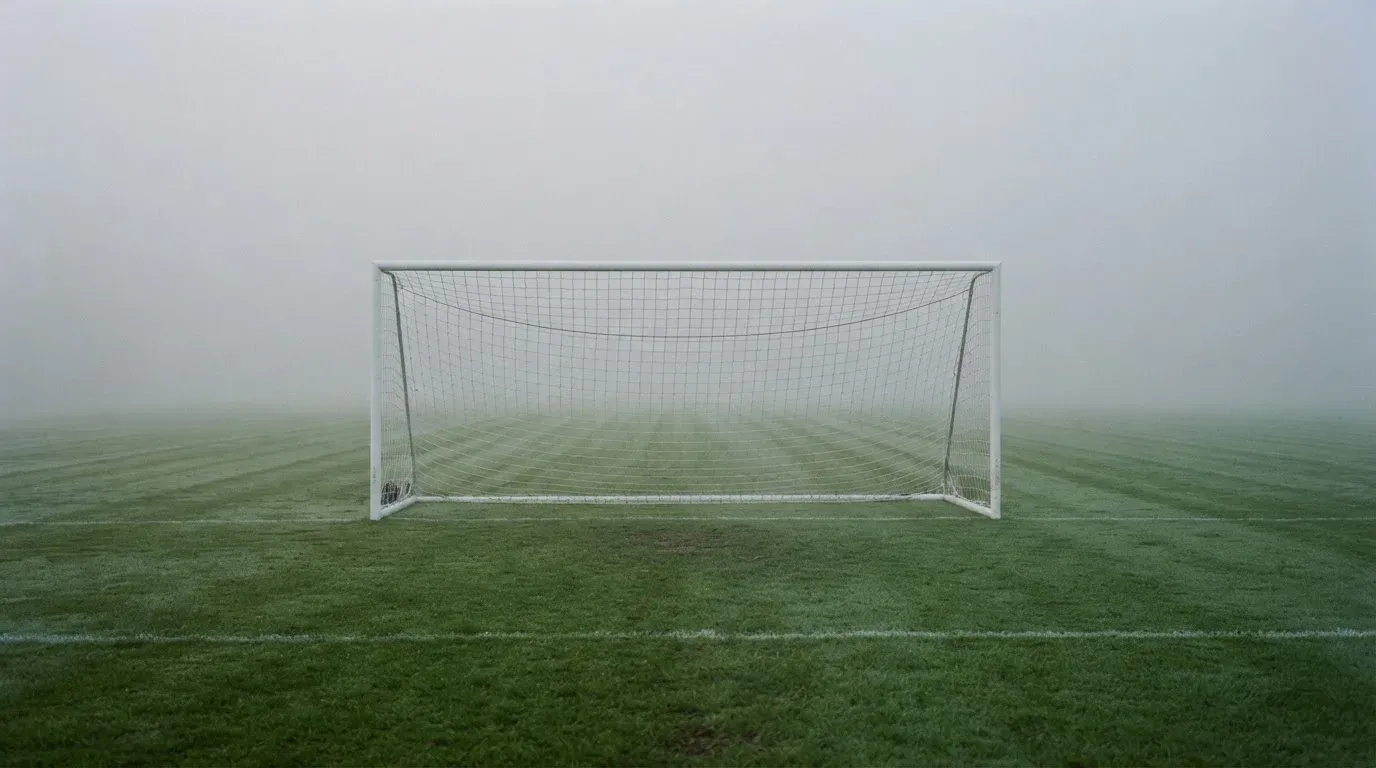 Eine Torlinie mit Netz steht am frühen Morgen im dichten Nebel auf einem Rasenplatz, die Umrisse der Pfosten verschwimmen.