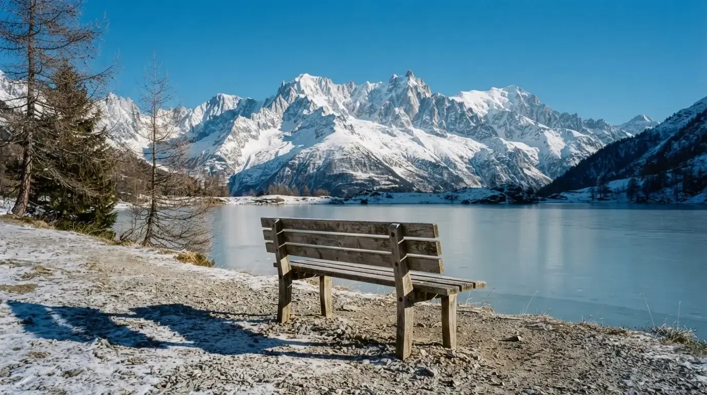 Eine Bank an einem Bergsee, dahinter schneebedeckte Gipfel im klaren Licht eines Wintermorgens.