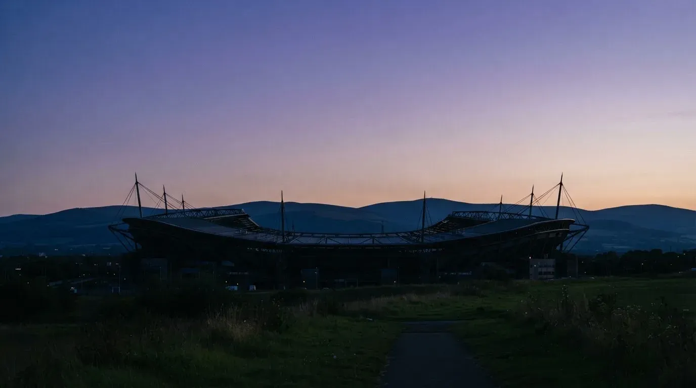 Die Silhouette eines Stadiondachs vor dem violetten Abendhimmel, dahinter eine Hügelkette.