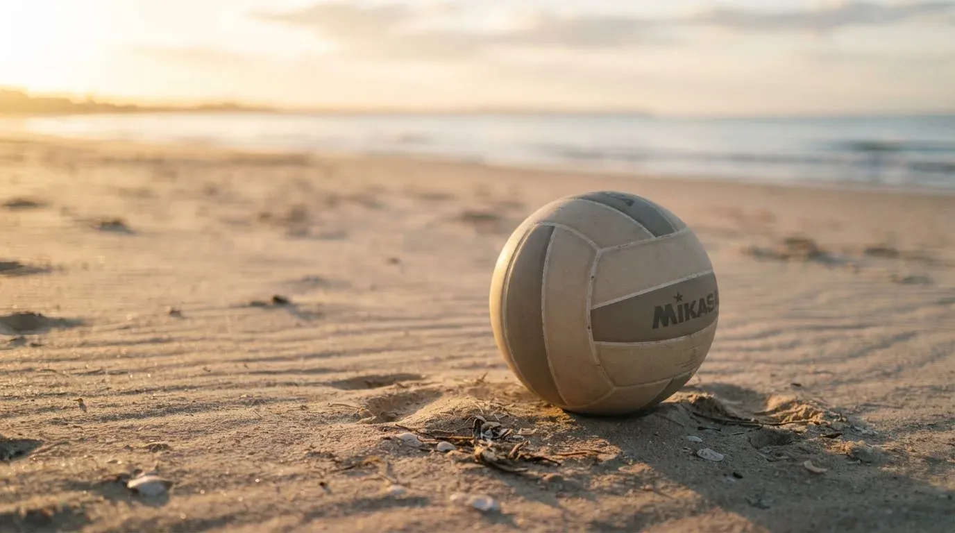 Ein Volleyball liegt auf feinem Sand an einem leeren Strand bei Sonnenaufgang.