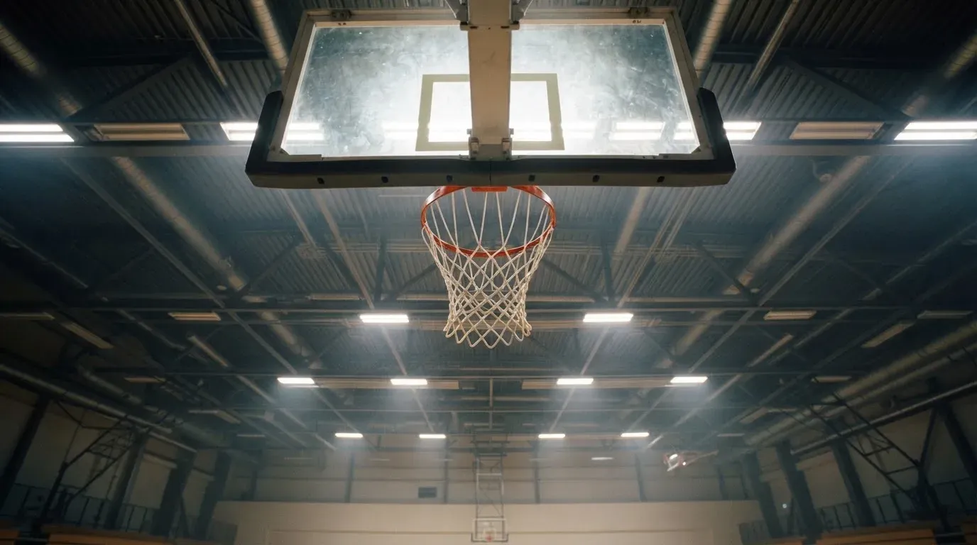 Ein Basketballkorb von unten gesehen, darüber eine Hallendecke mit Scheinwerfern und Stahlträgern.