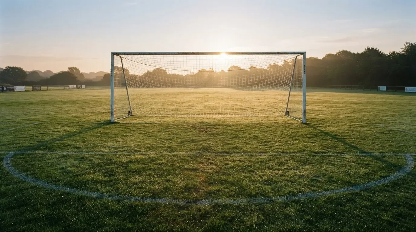 Ein Fussballtor mit Netz in der Totalen auf einem leeren Platz, Tau glänzt im Gras und die Morgensonne steht tief.