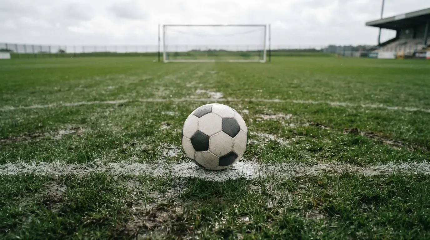 Ein einzelner Fussball liegt auf dem Elfmeterpunkt eines leeren Strafraums, der Rasen glänzt nass.
