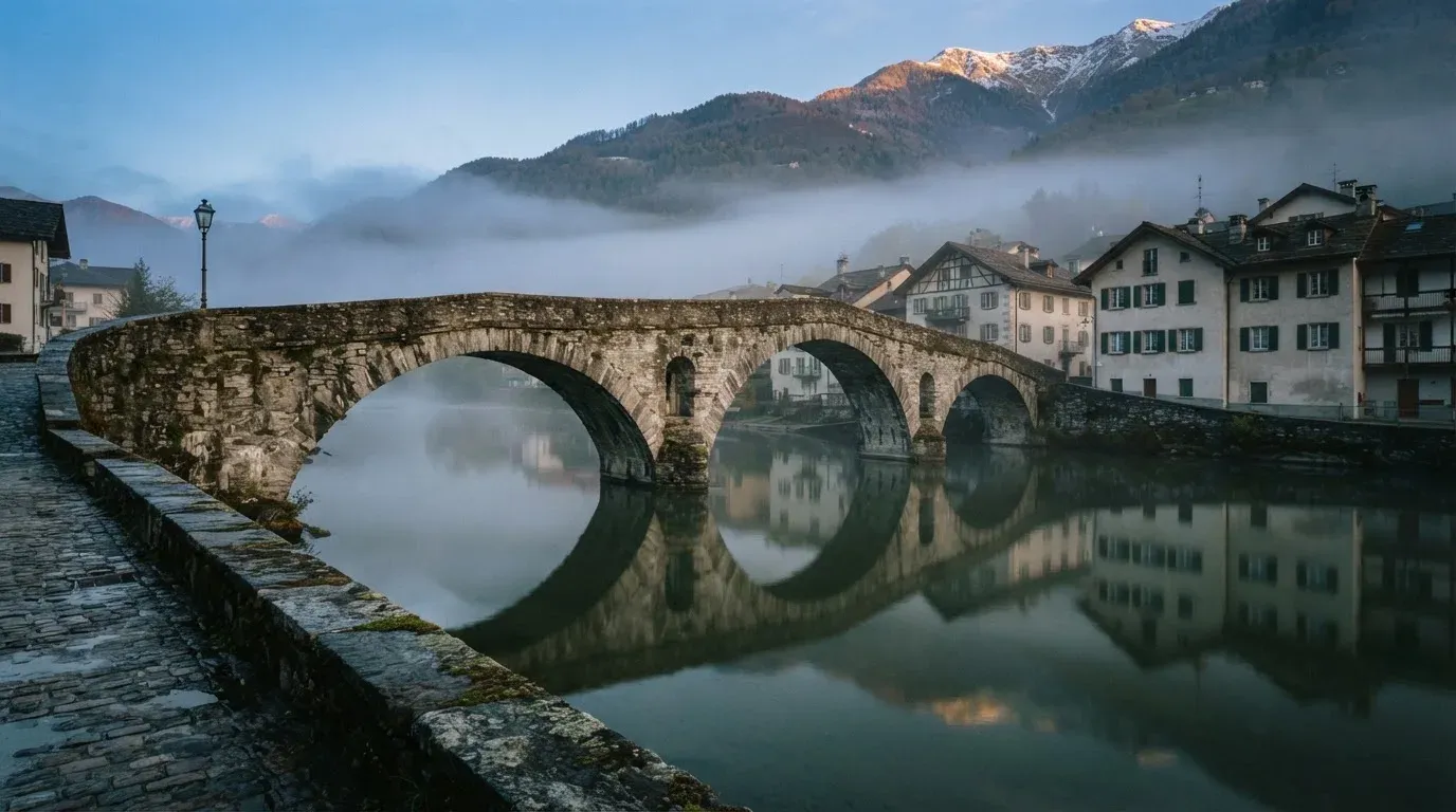 Eine steinerne Brücke über einen Fluss in einer Kleinstadt am frühen Morgen, Nebel zieht zwischen den Dächern hindurch