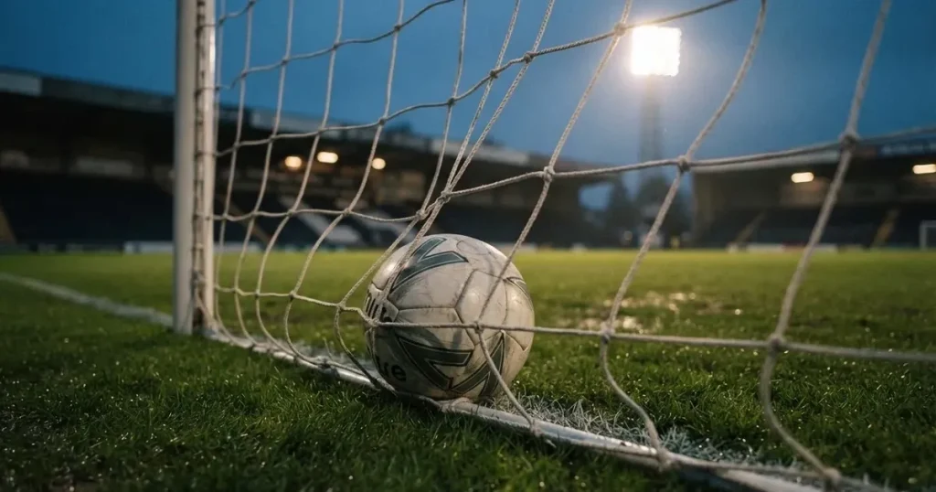 Ein Fussball liegt im Netz eines Tores, Flutlicht und kalte Abendluft liegen über dem leeren Platz