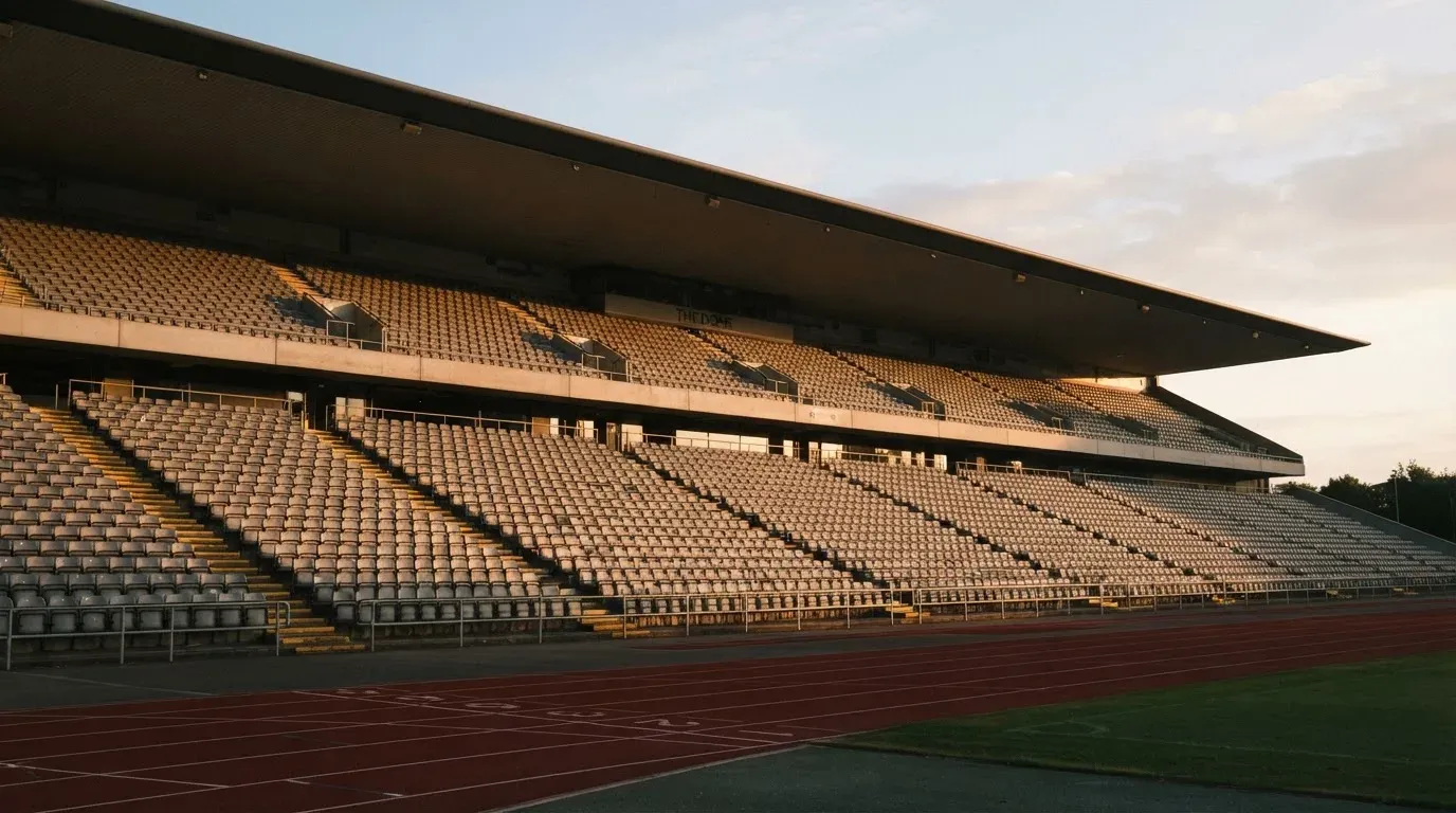 Eine leere Stadiontribüne bei Sonnenaufgang aus der Ferne, lange Schatten fallen über die Sitzreihen