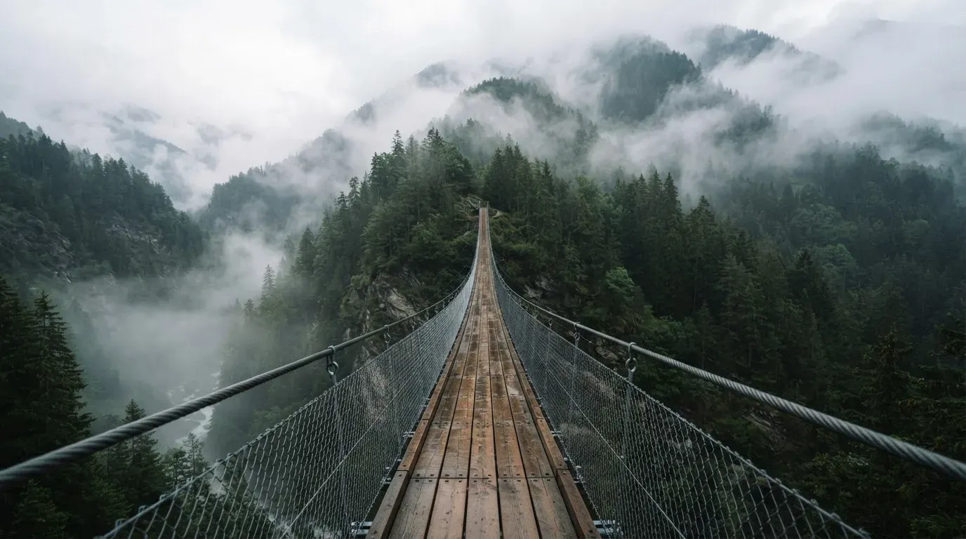 Eine Hängebrücke über eine Schlucht, Nebel steigt auf, dichter Wald bedeckt die steilen Hänge