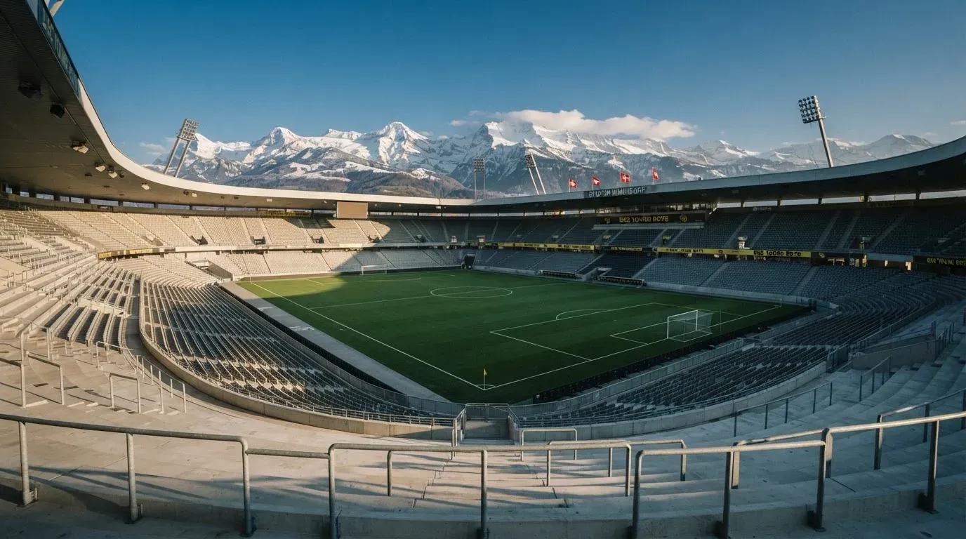 Schneebedeckte Berggipfel erheben sich im klaren Morgenlicht hinter einem leeren Stadion mit hellen Zuschauerrängen.