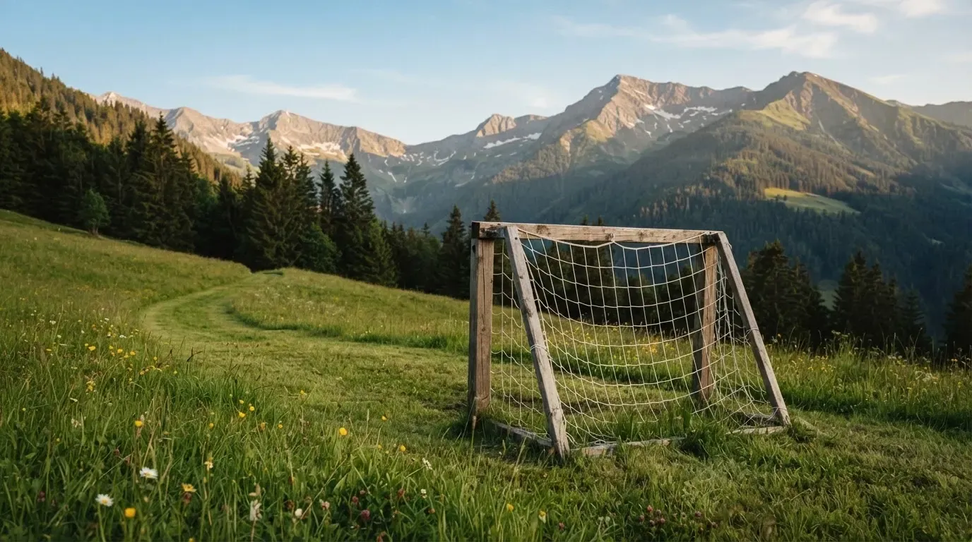 Eine Almwiese mit einem kleinen Holztor für Kinderfussball, dahinter erheben sich bewaldete Hänge im Nachmittagslicht.