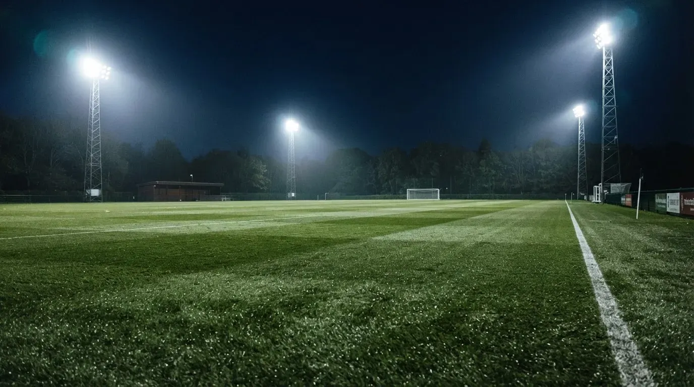 Hohe Flutlichtmasten ragen nachts über einen leeren Trainingsplatz, der Rasen glänzt im weissen Licht.