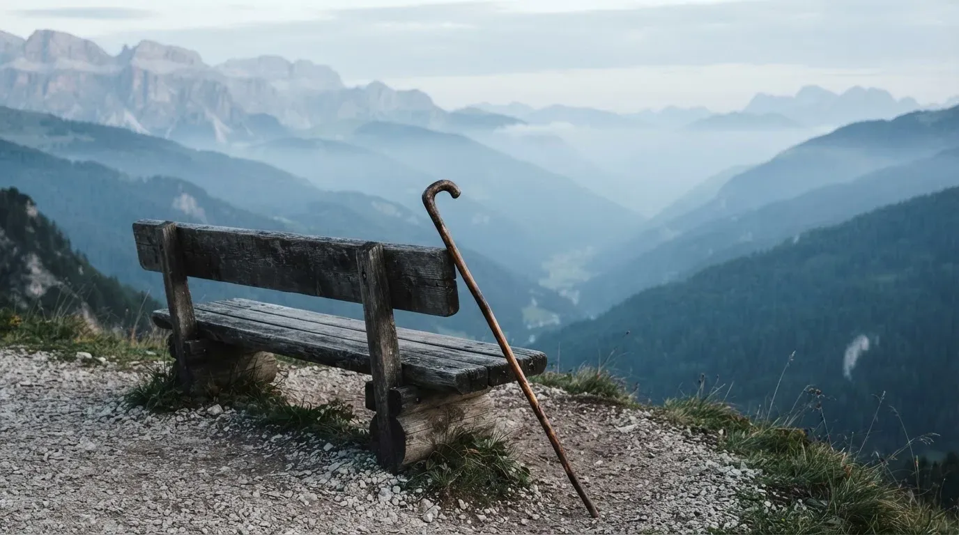 Ein Wanderstock lehnt an einer Holzbank auf einem Aussichtspunkt, dahinter breitet sich ein Tal im Dunst aus.